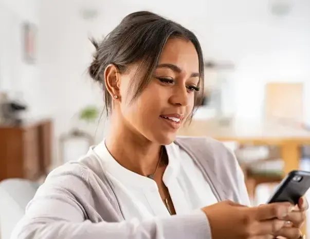 Woman smiling while looking at smartphone in bright indoor setting